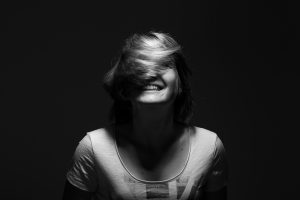 photo noir et blanc d'une femme qui rit à pleine dents, avec les cheveux qui se plaquent sur les yeux dans un mouvement de rotation