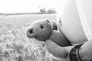 photographie d'un ventre de femme enceinte et un ourson en peluche, photo en noir et blanc